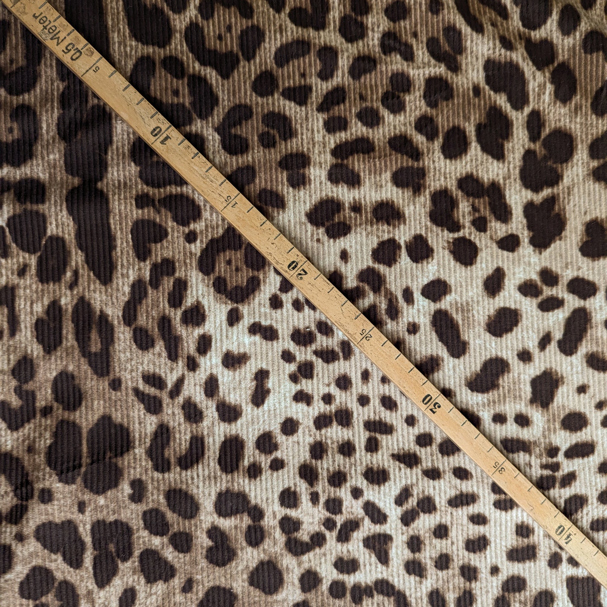 D&G deadstock corduroy fabric with a brown leopard print and a wooden measuring tape.