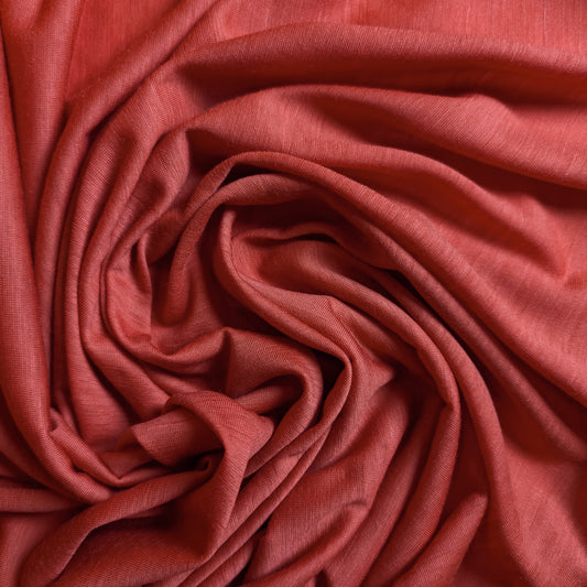 Soft coral red wool jersey fabric, draped in a swirl, showing its smooth texture.
