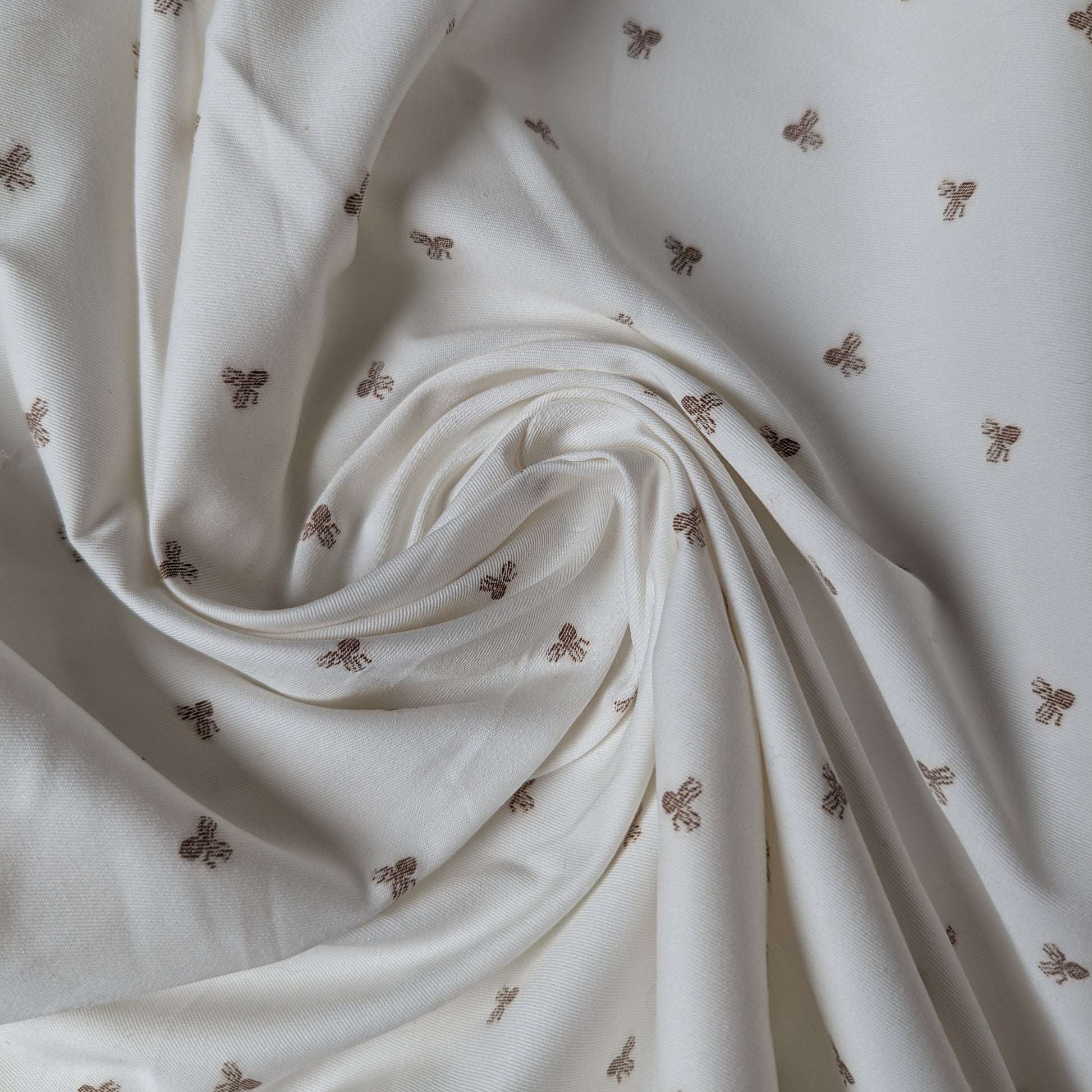 White deadstock cotton fabric with subtle brown octopus fil coupé design, draped.
