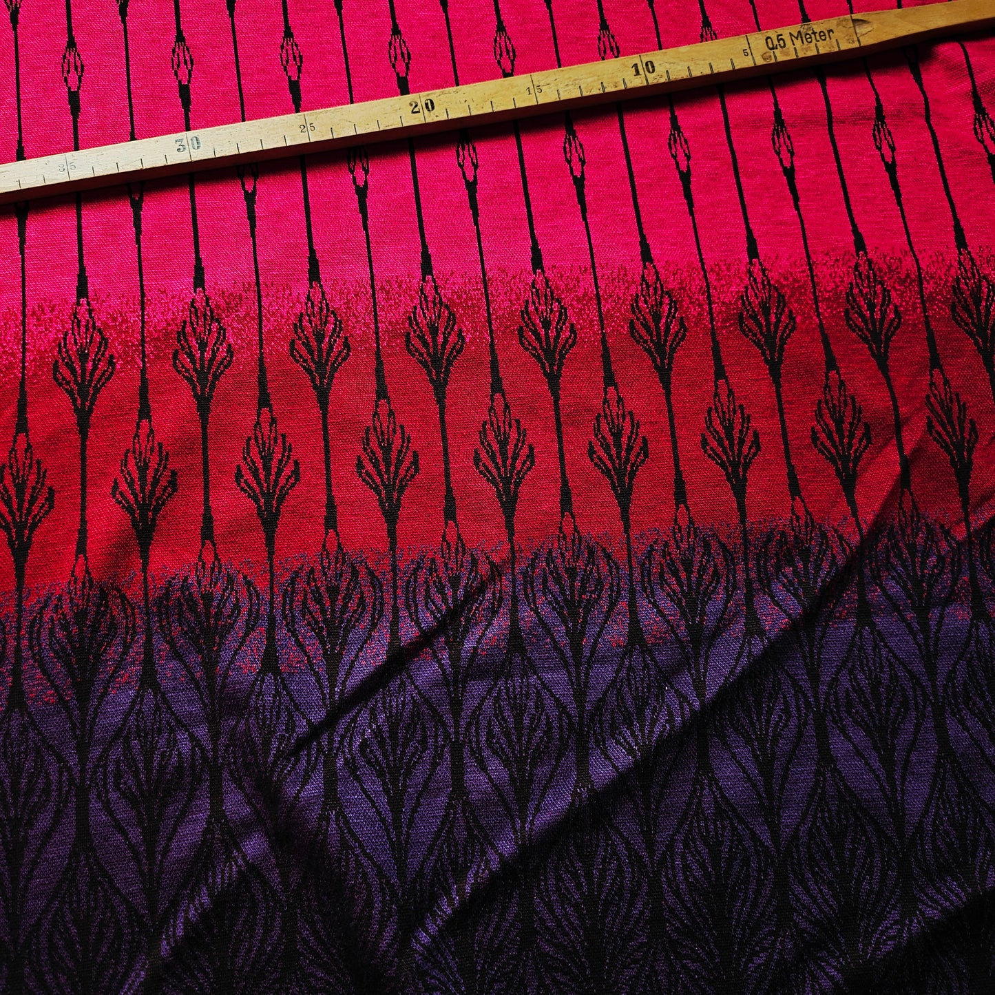 Deadstock jersey doubleface fabric in pink, red, and purple gradient with black leaf-like patterns.