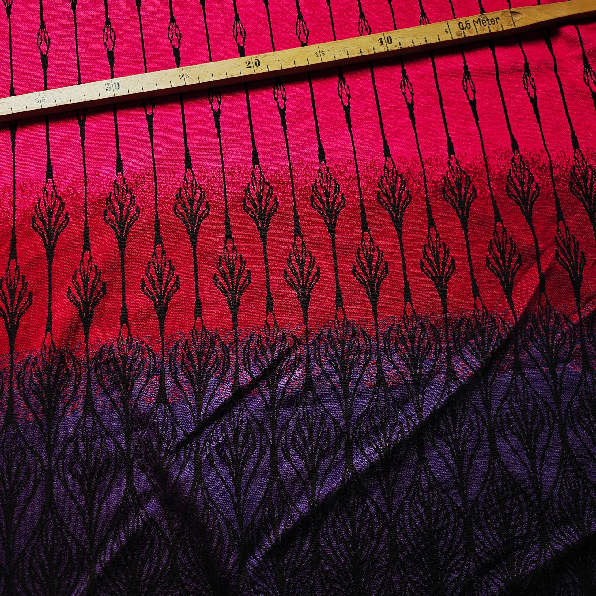 Deadstock jersey doubleface fabric in pink, red, and purple gradient with black leaf-like patterns.
