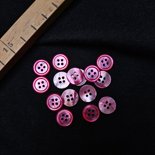Set of 15 pink mother-of-pearl 4-hole buttons, approx. 1 cm, on black fabric with a ruler.