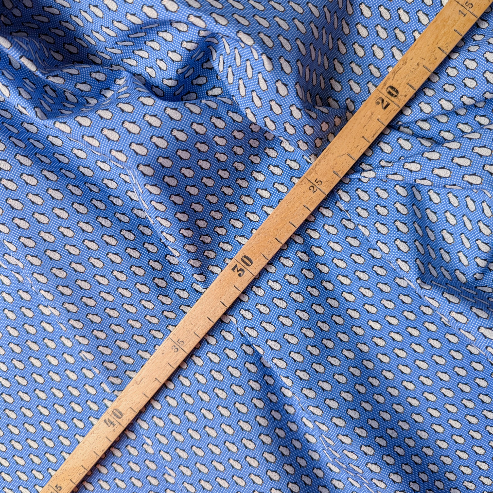 Designer deadstock blue cotton poplin fabric with white penguin pattern, measured by a wooden ruler.
