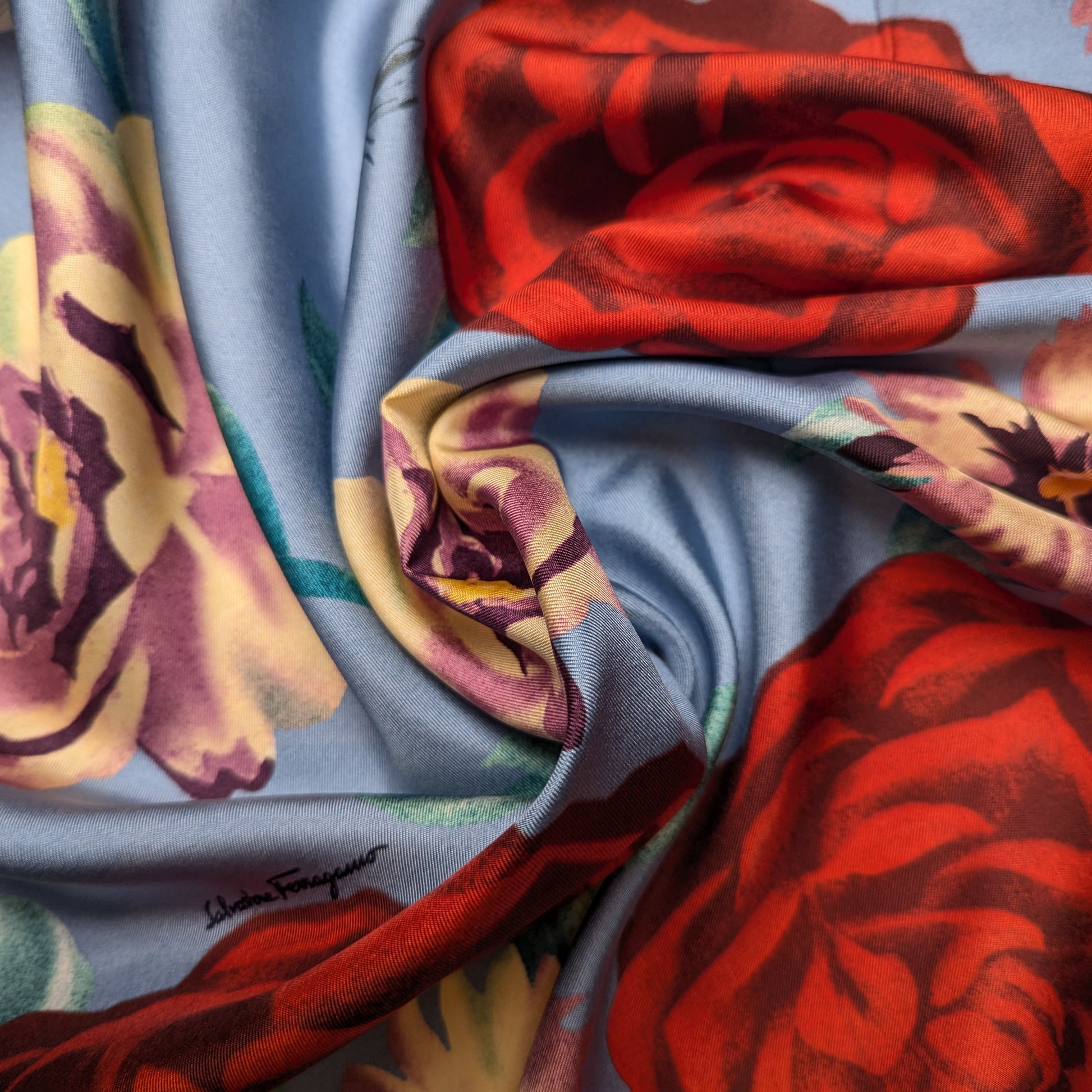 Light blue silk twill fabric with large red and yellow floral print, featuring a subtle designer logo.
