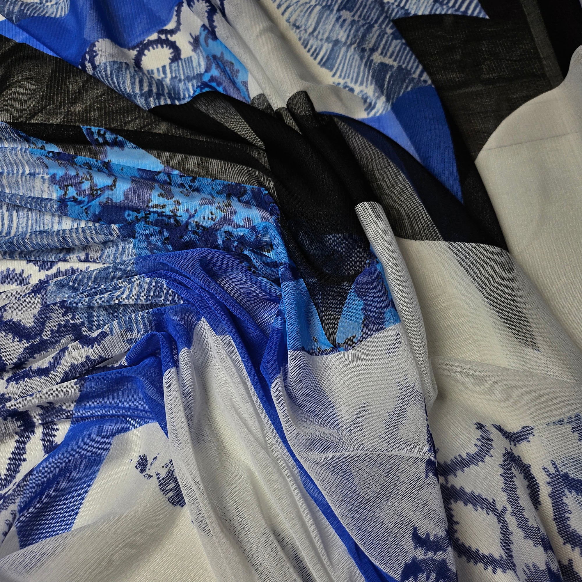 Bright white fine tulle designer fabric with abstract blue and black print, draped to show its sheer quality.