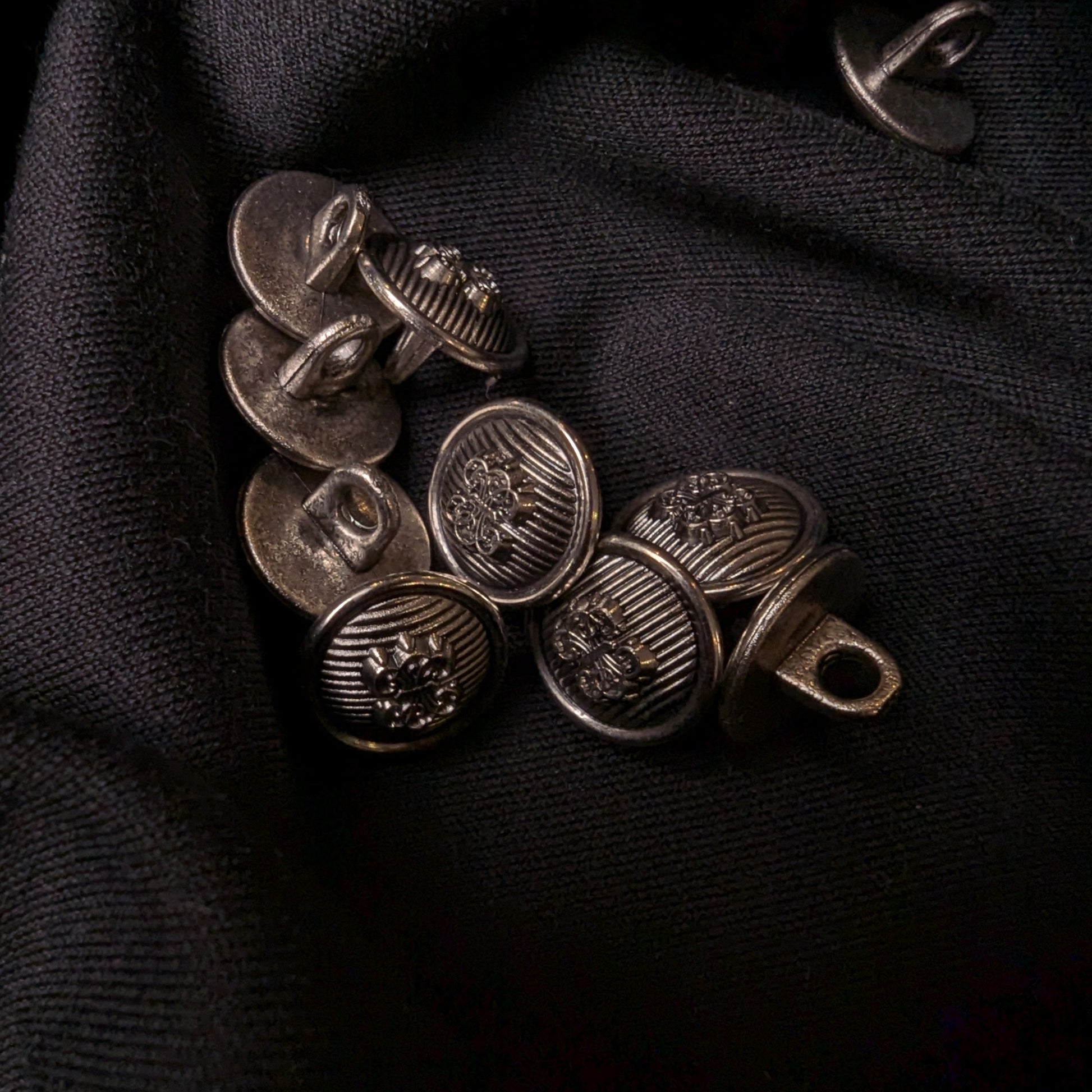 1.5 cm antique silver plastic buttons with textured designs on dark fabric.