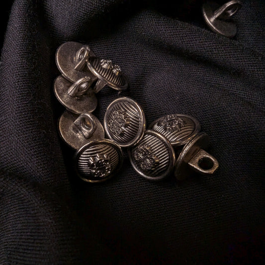 1.5 cm antique silver plastic buttons with textured designs on dark fabric.