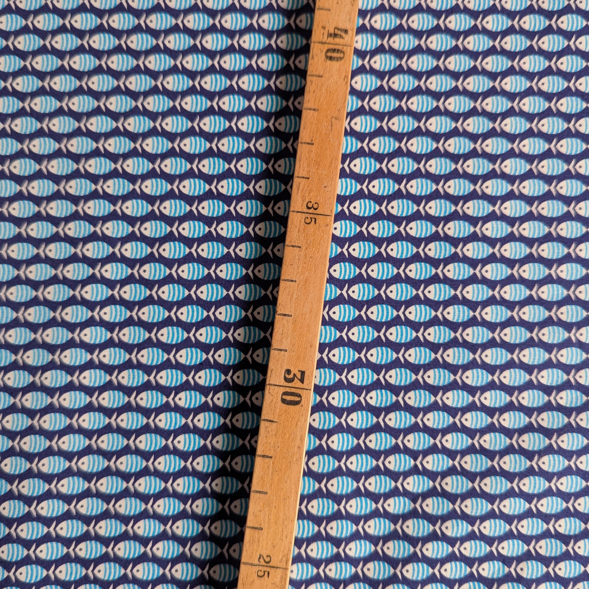 Dark blue cotton poplin fabric with light blue fish pattern, measured by a wooden ruler.