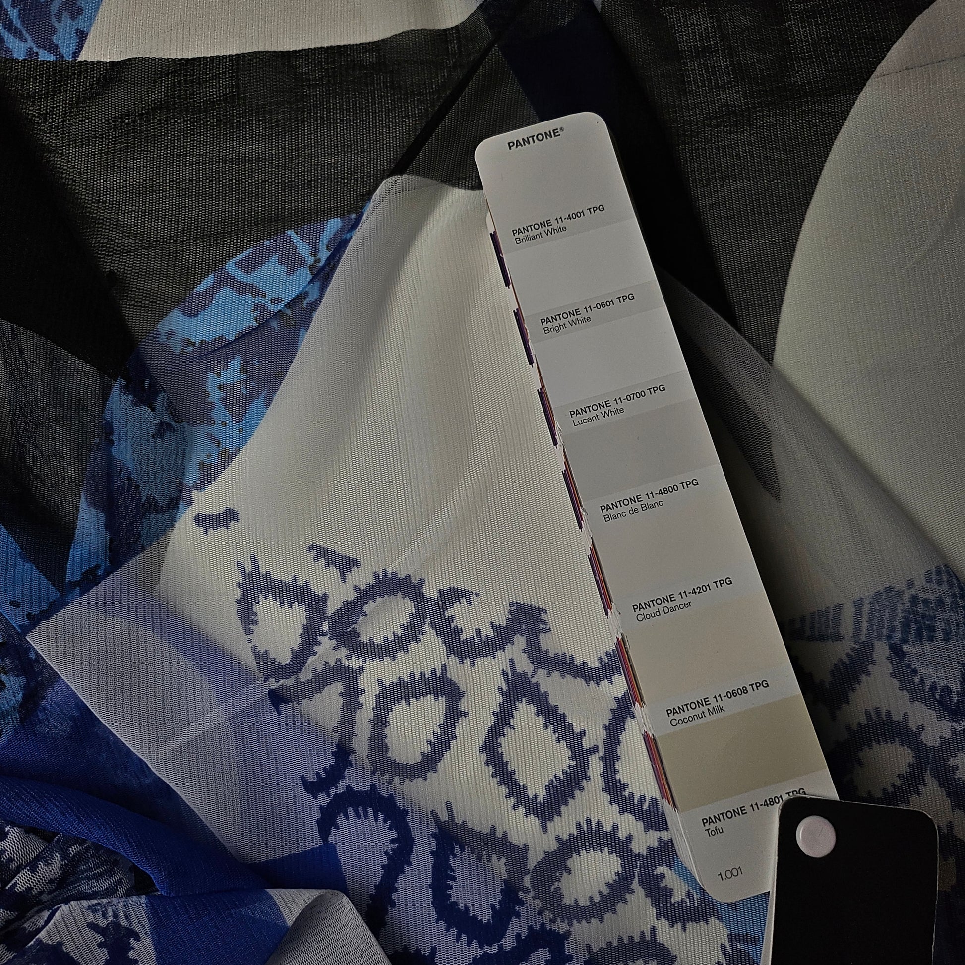 Bright white designer deadstock fine tulle fabric with abstract blue print, 185 cm wide, shown with Pantone swatch.