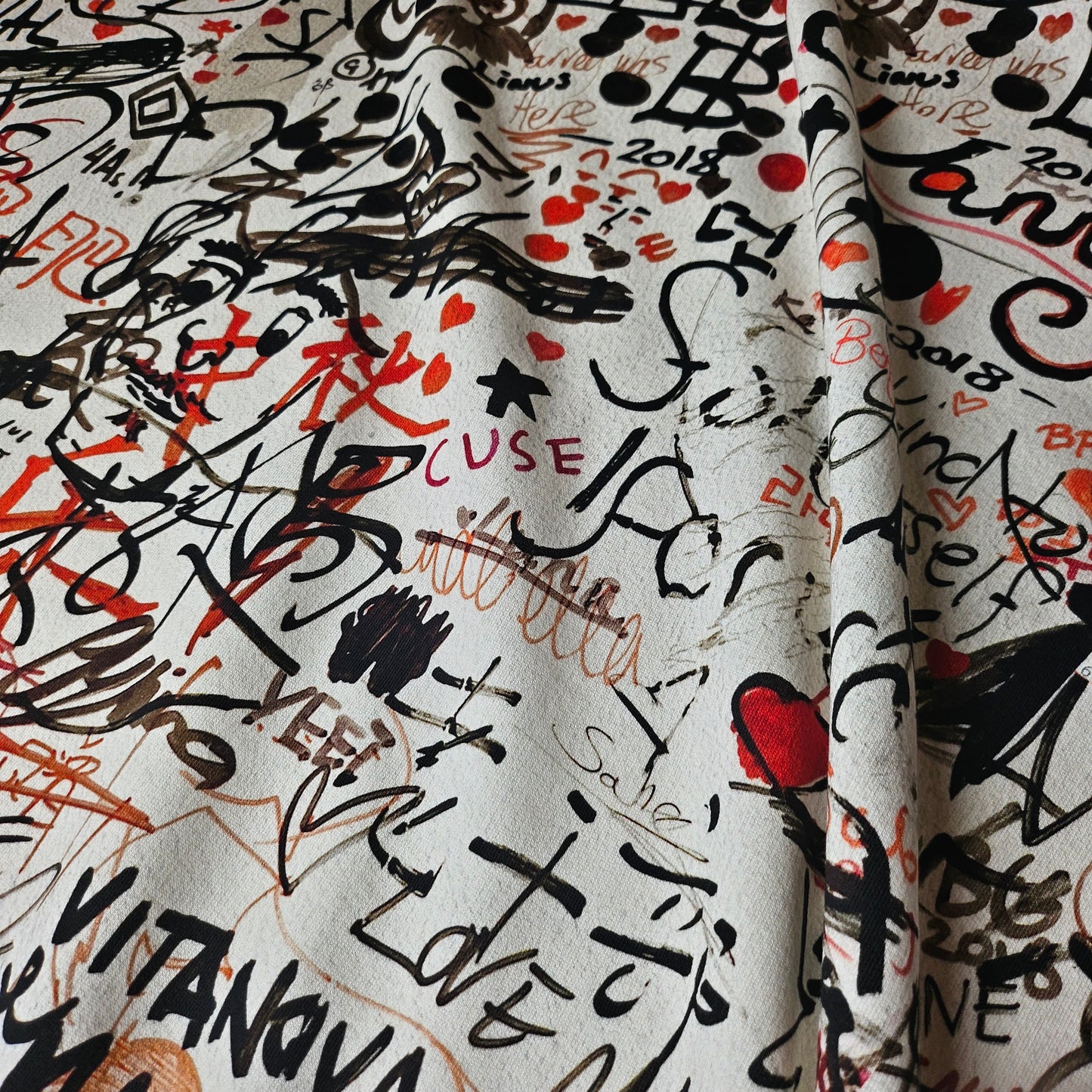 White deadstock Burberry sweat panel fabric with black, red, and brown graffiti-style script and heart patterns.