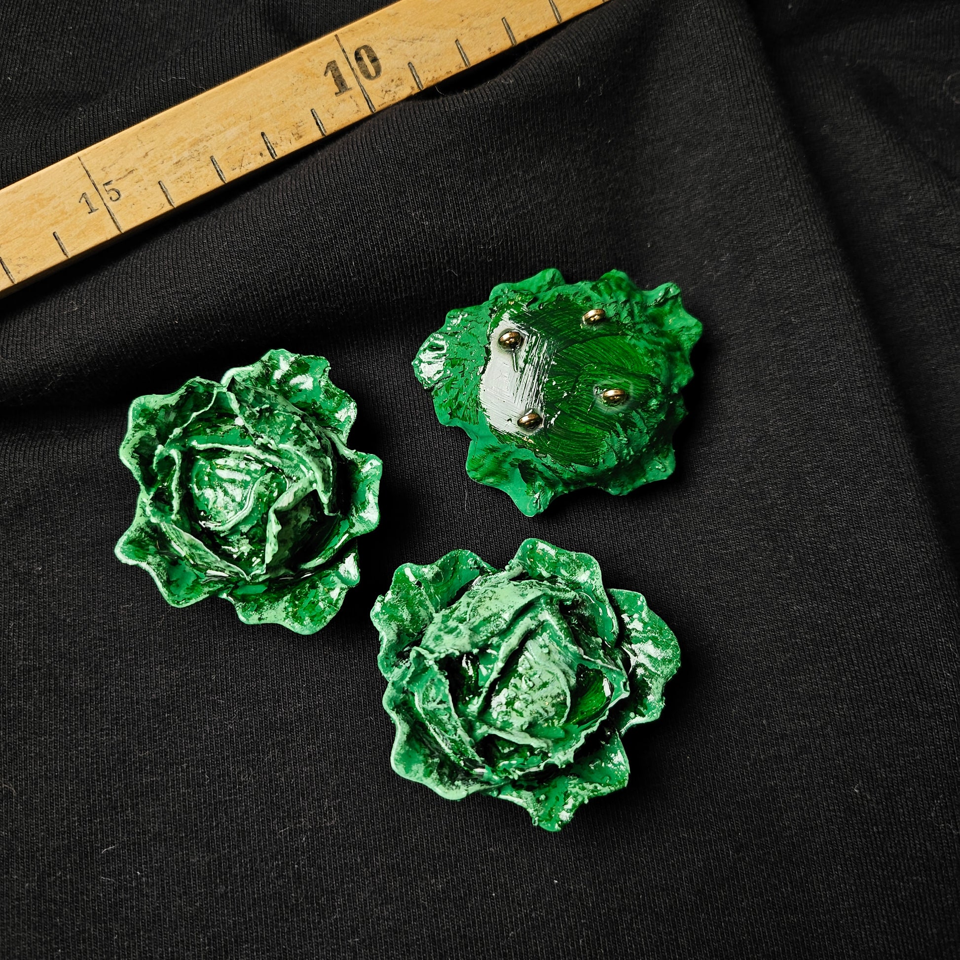 Three D&G green plastic cabbage-shaped appliques, 4x4cm, on black fabric with a ruler.