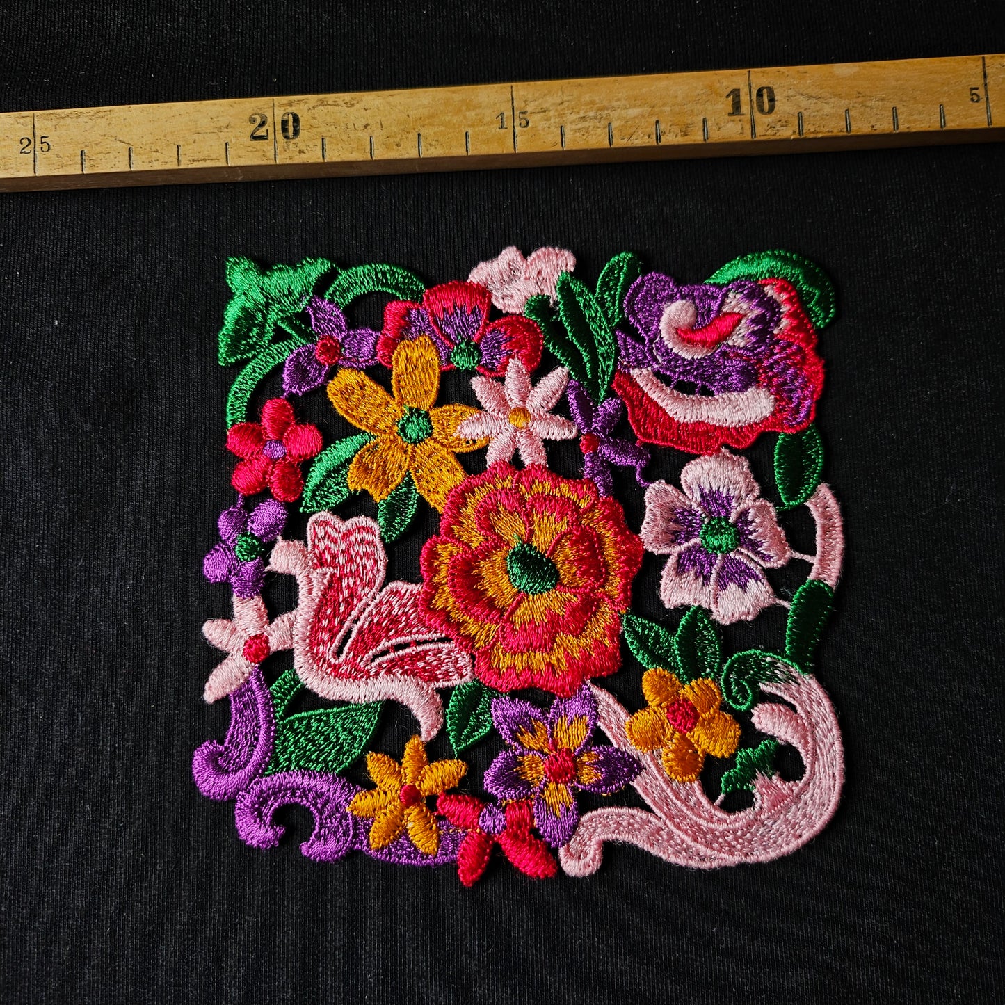 Colorful embroidered floral patch, 12cm x 12cm, on black fabric with a ruler.