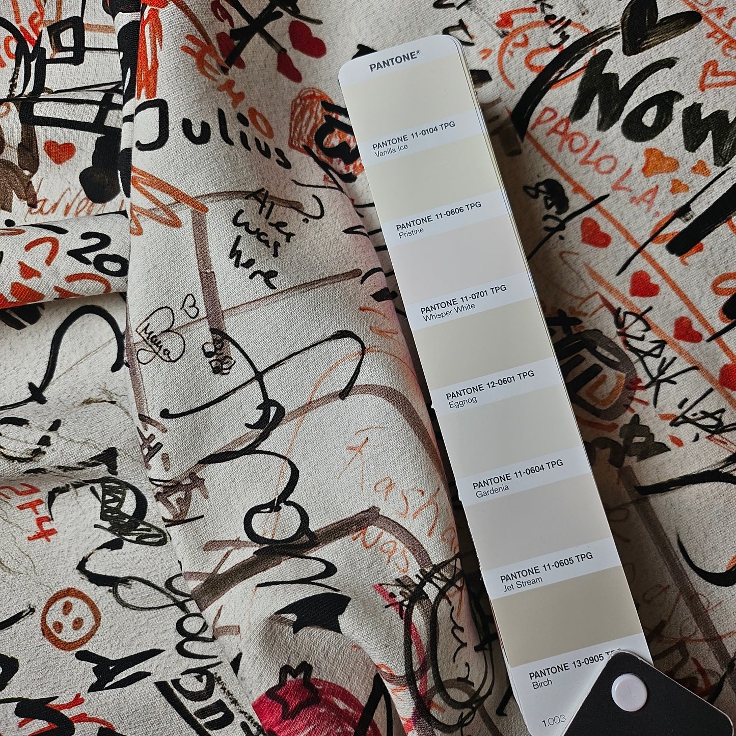 Deadstock B*rberry sweat panel in Whisper White with black, red, and brown graffiti-style print, next to a Pantone color swatch.
