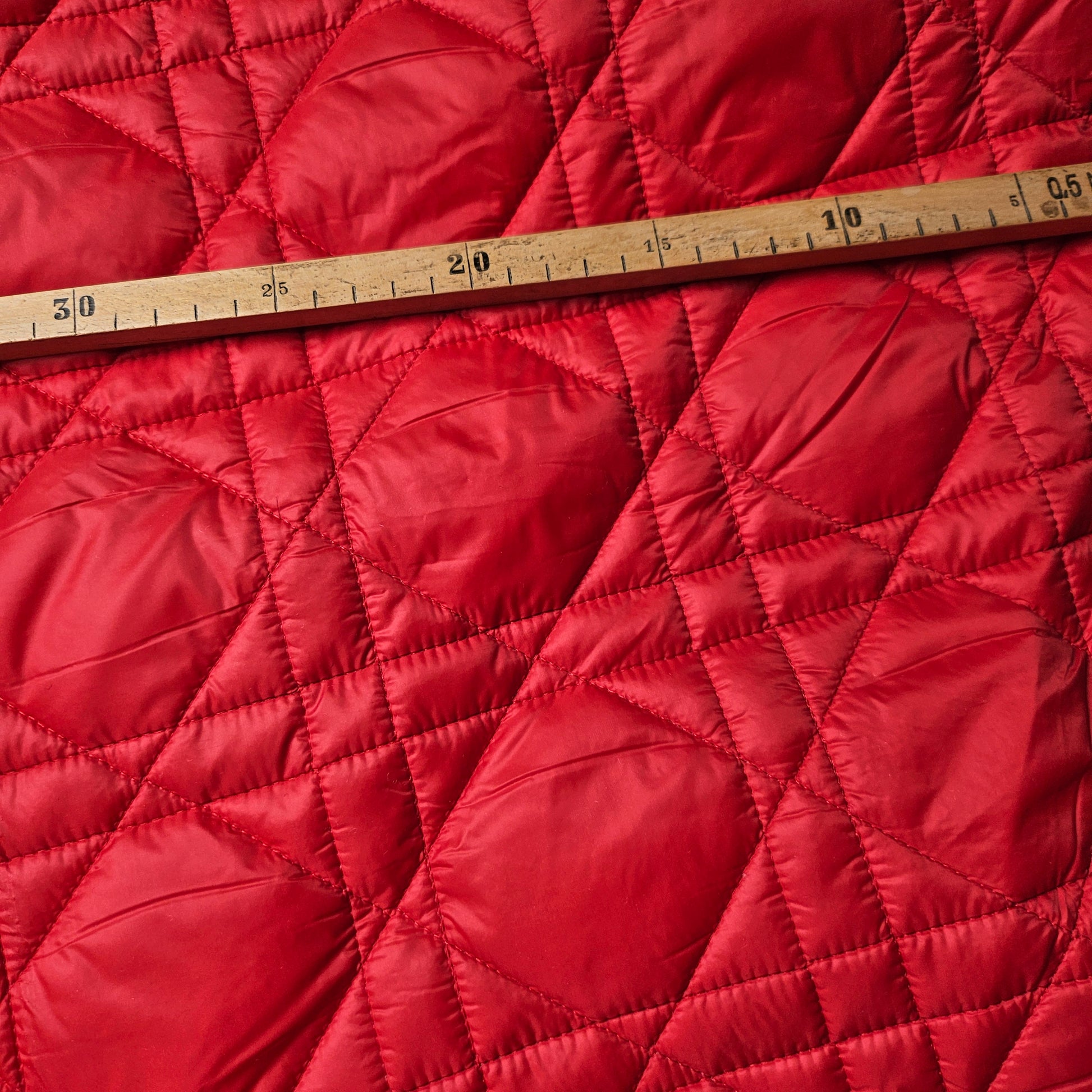 Tomatenrot D*or deadstock quilted fabric with macrocannage pattern and wooden ruler.