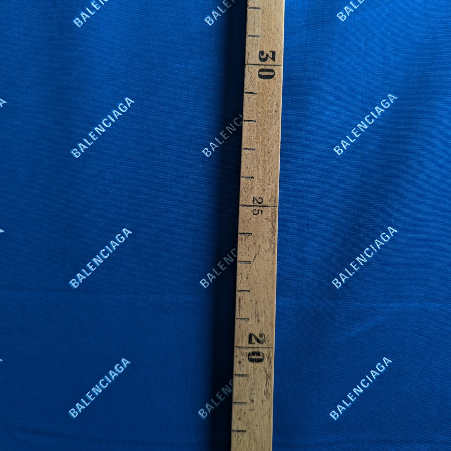 Blue Balenciaga cotton poplin fabric with white logo print, measured by a wooden ruler.